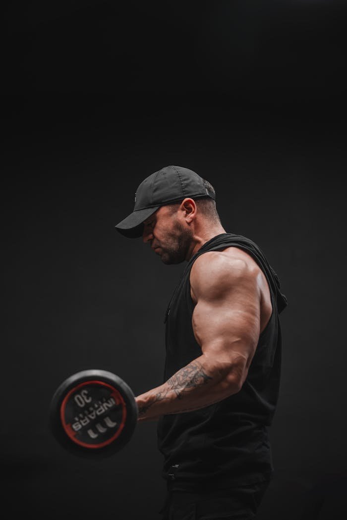 Muscular man lifting a dumbbell in a dark gym environment.